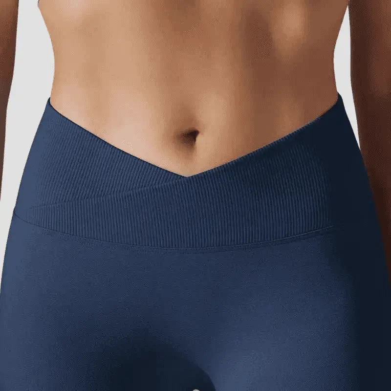 Une vue rapprochée mettant en valeur le design ergonomique d'un legging de sport bleu marine. L'image se focalise sur la ceinture haute croisée en forme de V, confectionnée dans un tissu à texture côtelée qui contraste avec la matière lisse de la jambe.